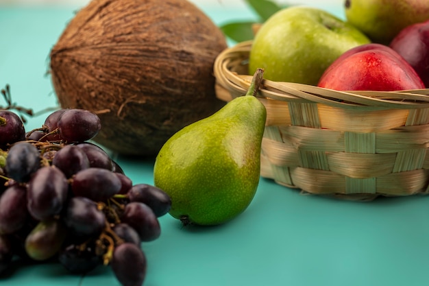 Vista cercana de frutas como uva pera coco y canasta de manzana melocotón sobre fondo azul.