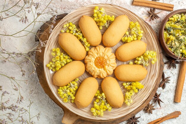 Vista cercana de galletas en bandeja de madera y diferentes hierbas en mármol blanco