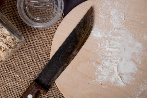 Vista cercana de harina blanca con cuchillo en tabla de cortar de madera sobre superficie de tela de saco