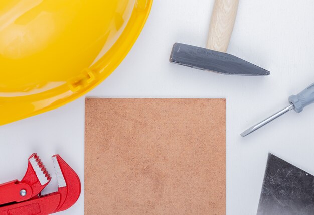 Vista cercana de herramientas de construcción como martillo de ladrillo casco de seguridad destornillador llave de tubo espátula alrededor de azulejo mettlach sobre fondo blanco