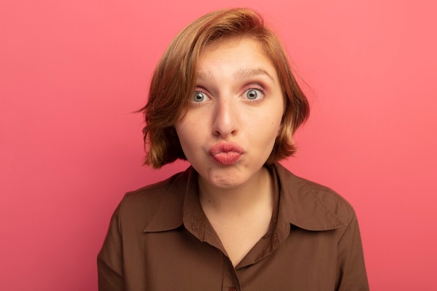 Vista cercana de impresionada joven rubia mirando haciendo gesto de beso aislado en la pared rosa