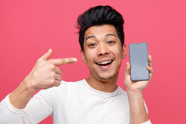 Vista cercana del joven emocionado sosteniendo y apuntando al teléfono móvil