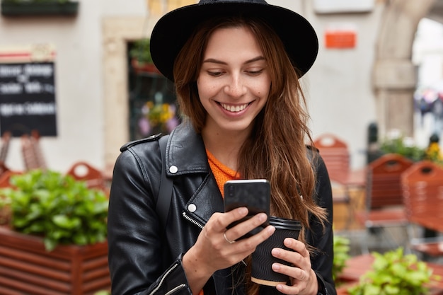 Vista cercana de la joven encantada utiliza la conexión a Internet de datos de teléfono móvil, lee un mensaje de texto