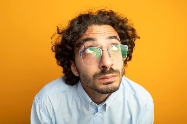 Vista cercana de joven guapo con gafas aislado en la pared naranja