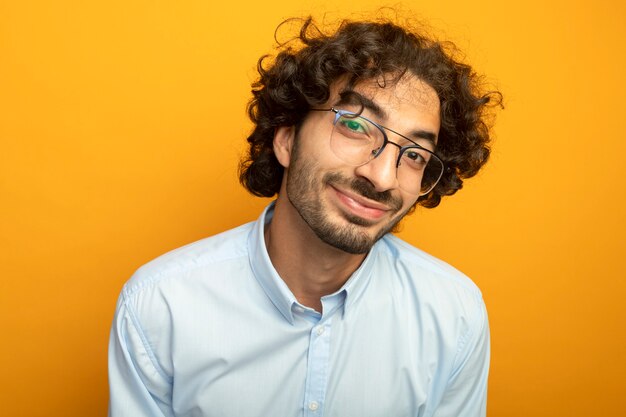 Vista cercana de joven guapo con gafas mirando al frente aislado en la pared naranja