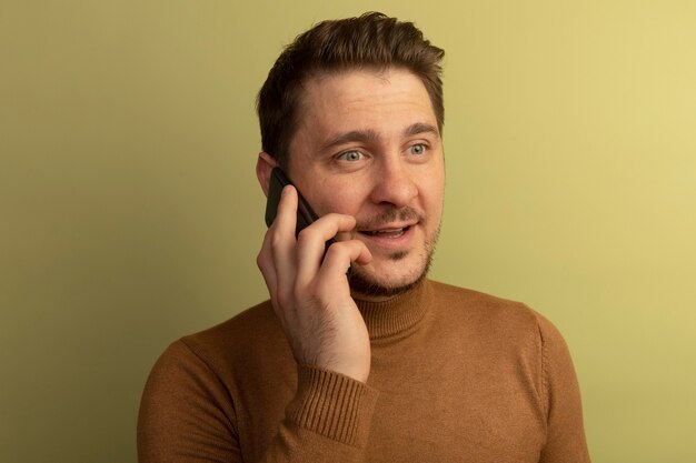 Vista cercana del joven guapo rubio complacido mirando directamente hablando por teléfono