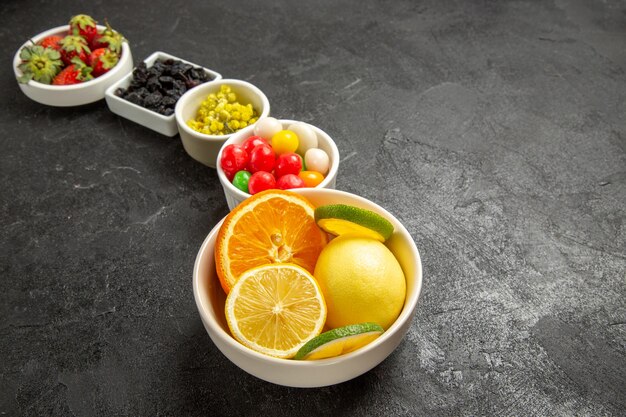 Vista cercana lateral apetitosas frutas y bayas tazones blancos de frutas cítricas fresas y dulces en la mesa negra