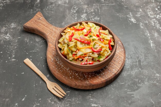 Vista cercana lateral ensalada ensalada de verduras en el recipiente marrón en el tenedor de madera de tablero de cocina