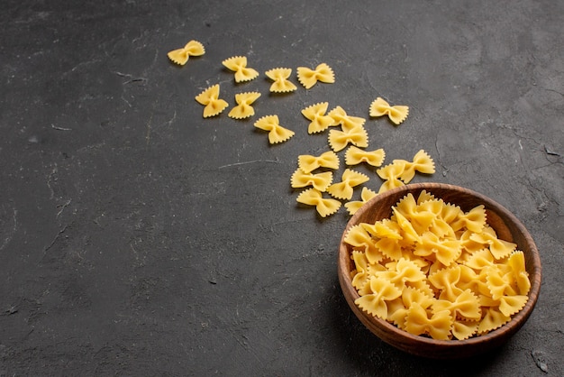 Vista cercana lateral pasta pasta en un tazón de madera en el lado derecho de la mesa oscura