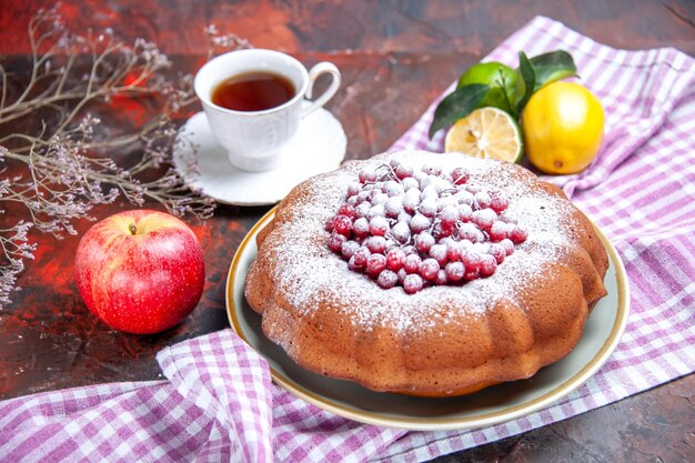 Vista cercana lateral un pastel un pastel con frutos cítricos sobre el mantel una taza de té
