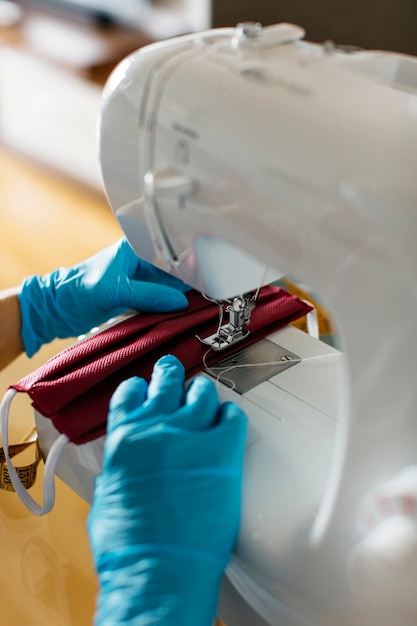 Vista cercana de manos cosiendo una mascarilla de tela con máquina de coser