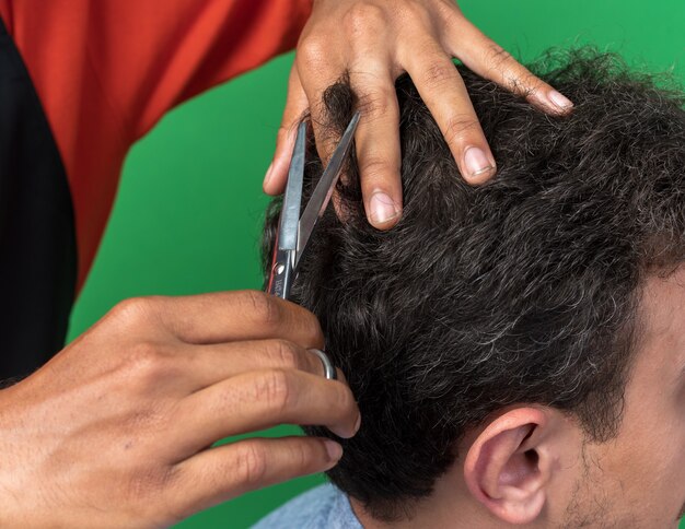 Vista cercana de las manos del peluquero masculino haciendo corte de pelo para su joven cliente