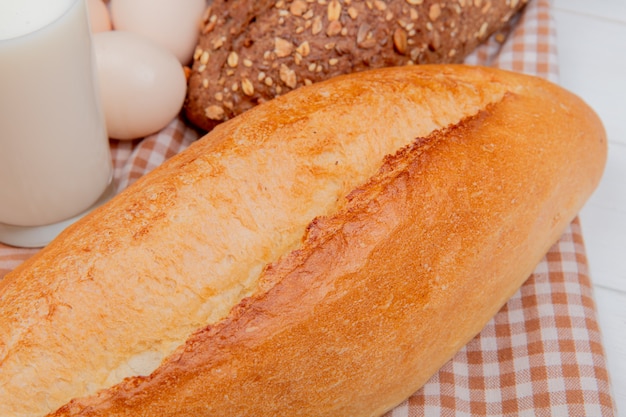 Vista cercana de panes como baguette vietnamita y con semillas negras con leche de huevos sobre tela escocesa y mesa de madera