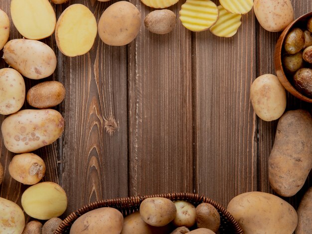 Vista cercana de papas enteras y en rodajas en forma circular sobre fondo de madera con espacio de copia