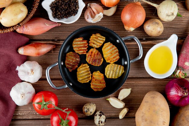 Vista cercana de papas fritas y verduras alrededor como tomate cebolla ajo con pimienta negra y mantequilla sobre fondo de madera