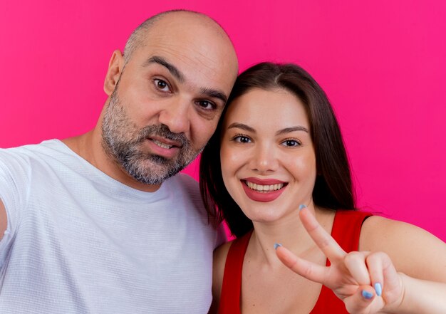 Vista cercana de la pareja adulta hombre confiado y mujer sonriente haciendo el signo de la paz ambos mirando