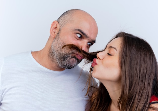 Vista cercana de la pareja adulta hombre juguetón haciendo bigote de cabello de mujer mirando a su mujer haciendo gesto de beso