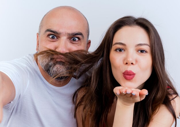 Vista cercana de la pareja adulta hombre juguetón haciendo bigote de cabello de mujer y mujer enviando beso de golpe