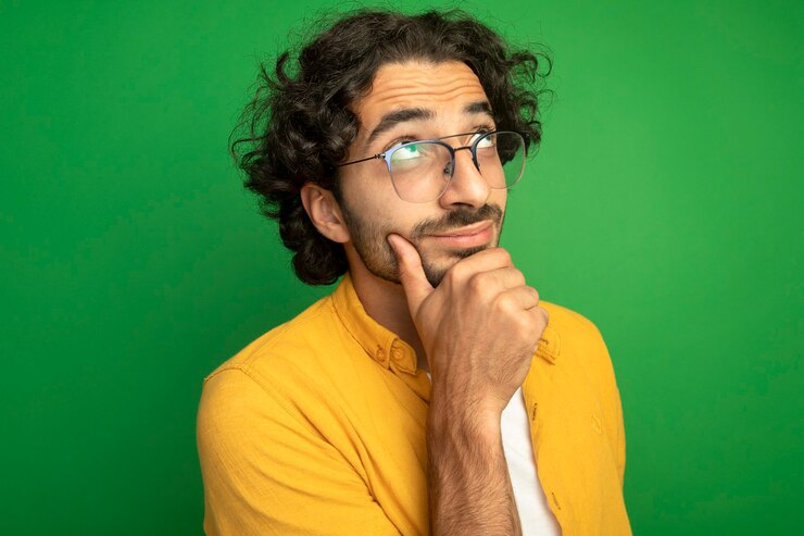 Foto gratuito vista cercana de pensativo joven guapo con gafas tocando la barbilla mirando hacia arriba aislado en la pared verde