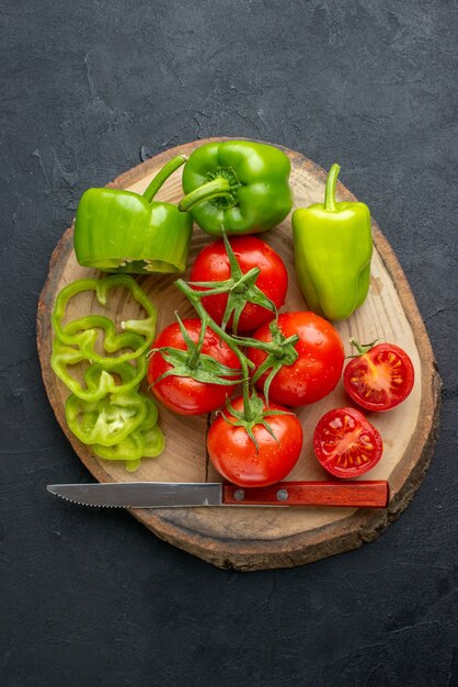 Vista cercana de pimientos verdes picados cortados enteros y tomates frescos en la tabla de cortar de madera sobre superficie negra