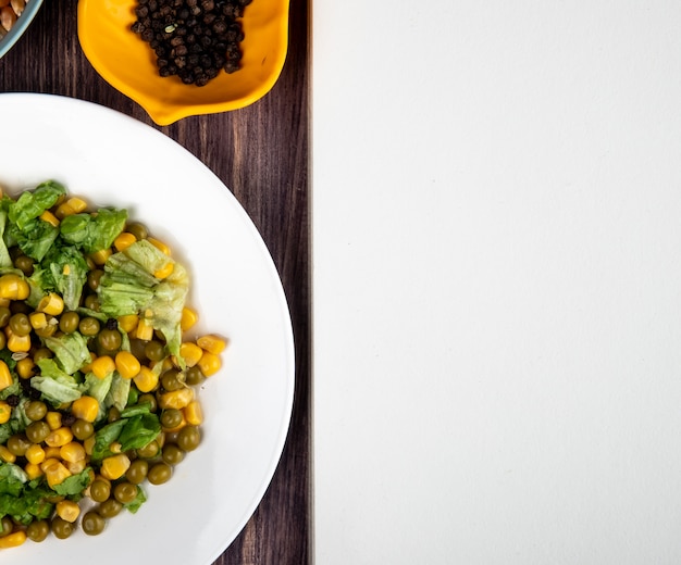 Vista cercana del plato de ensalada de maíz con semillas de pimienta negra sobre superficie de madera con espacio de copia