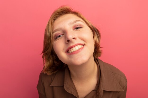 Vista cercana de la sonriente joven rubia mirando aislado en la pared rosa