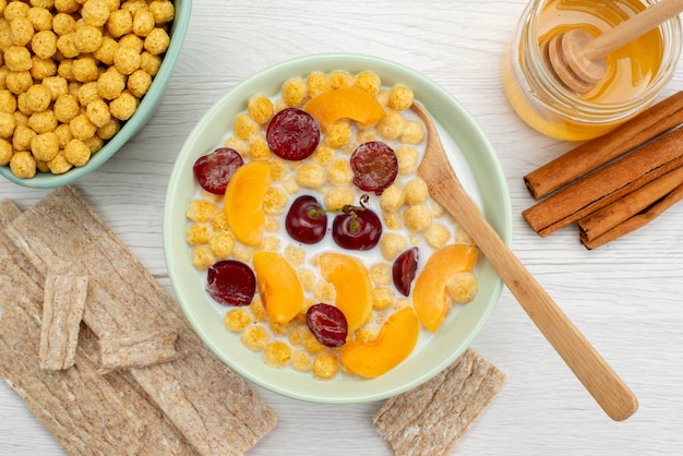 Vista cercana superior cereales con leche dentro de un plato con galletas de canela y miel en blanco, beber leche lácteos, crema de desayuno