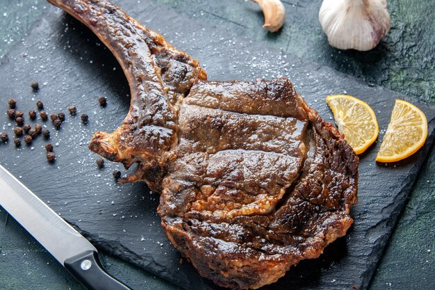 Vista cercana superior rebanada de carne frita con rodajas de limón sobre una superficie oscura