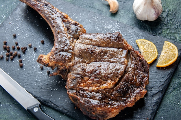 Vista cercana superior rebanada de carne frita con rodajas de limón sobre una superficie oscura