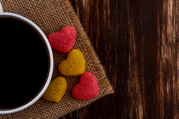 Vista cercana de la taza de té y mermelada sobre tela de saco y fondo de madera con espacio de copia