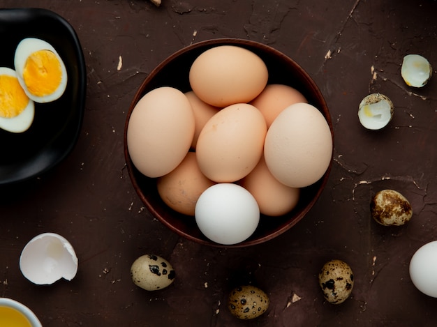 Vista cercana del tazón de huevos con otros huevos alrededor sobre fondo marrón