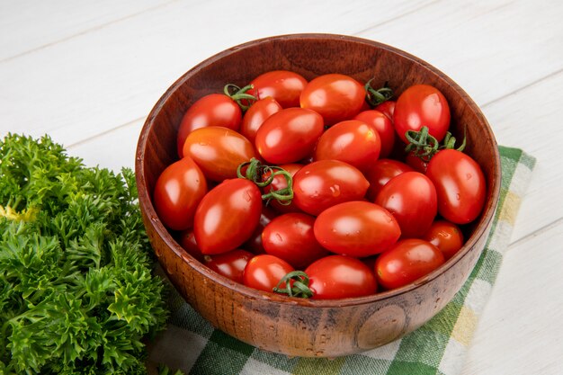 Vista cercana de tomates en un tazón con cilantro chino sobre tela en mesa de madera