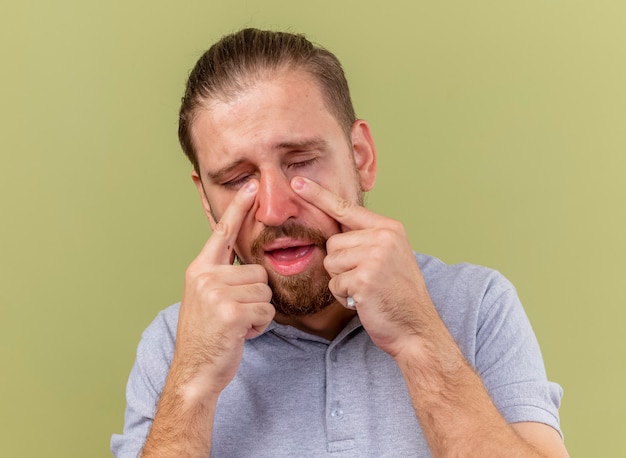 Vista cercana de triste joven apuesto enfermo eslavo sosteniendo la servilleta poniendo los dedos debajo de los ojos con los ojos cerrados aislados en la pared verde oliva