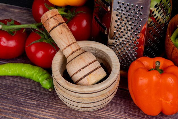 Vista cercana de la trituradora de ajo con rallador y verduras como tomate y pimiento en mesa de madera