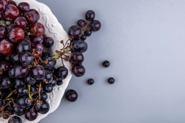 Vista cercana de uvas negras y rojas en placa sobre fondo gris con espacio de copia