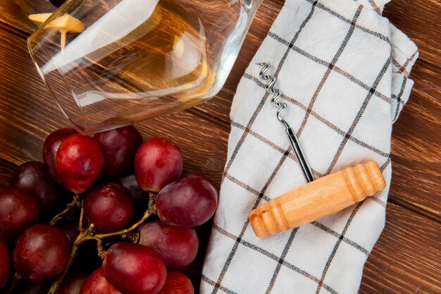 Foto gratuita vista cercana de vaso de vino blanco y uva con sacacorchos sobre tela en mesa de madera