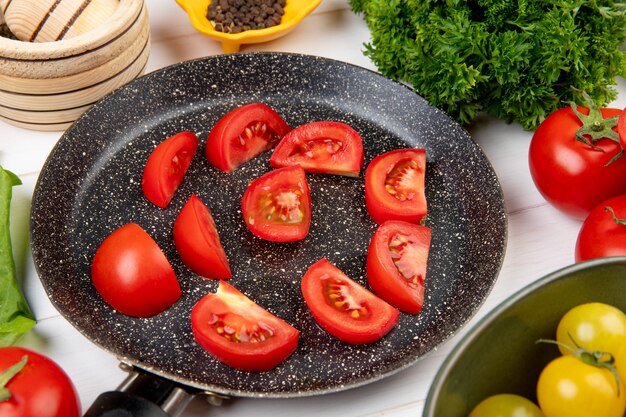 Vista cercana de vegetales como semillas de tomate pimienta negra cilantro con rodajas de tomate en sartén sobre mesa de madera