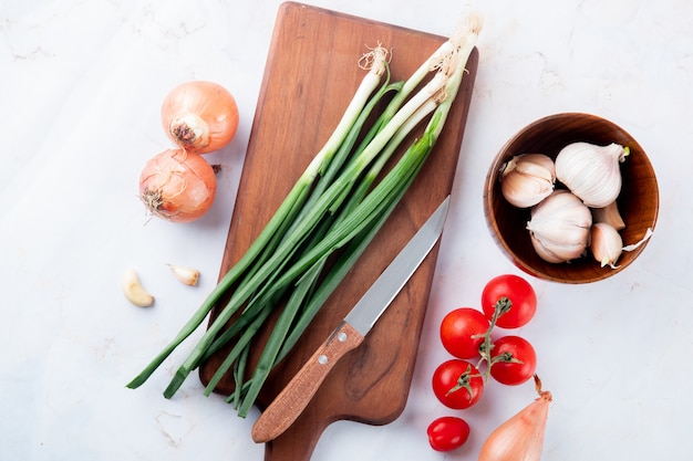 Vista cercana de verduras como cebolla ajo tomate con tabla de cortar y cuchillo sobre fondo blanco con espacio de copia