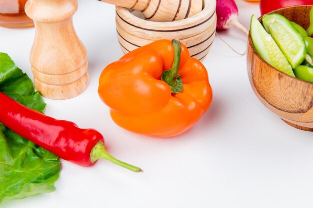 Vista cercana de verduras como pimiento rábano tomate con ensalada de verduras sal pimienta negra y dejar en mesa blanca