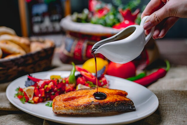 Vista cercana de verter salsa de granada sobre salmón al horno servido con vegetales frescos