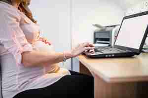 Foto gratuita vista de cintura de una mujer embarazada usando la computadora portátil en el escritorio de madera