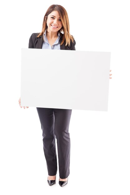 Vista completa de una hermosa joven empresaria hispana sosteniendo un gran cartel contra un fondo blanco y sonriendo