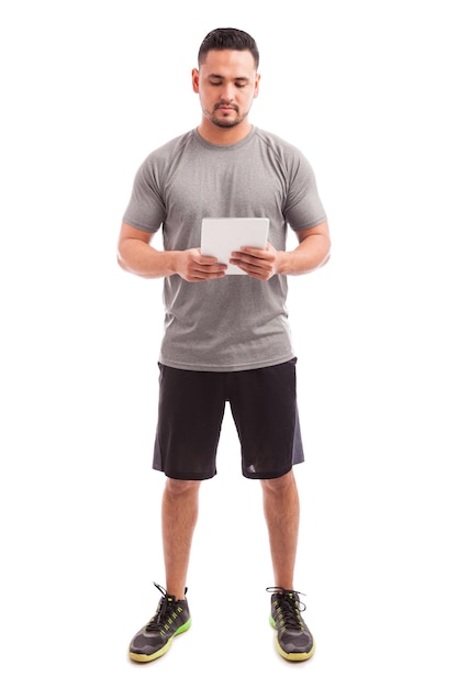 Vista completa de un joven instructor de fitness que usa una tableta para encontrar la rutina perfecta