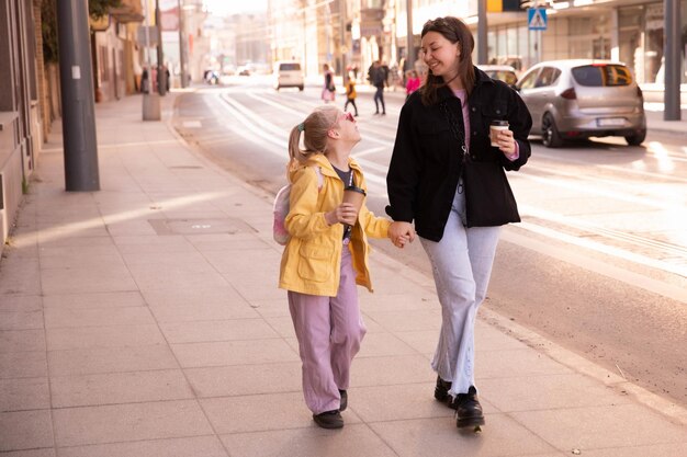 Vista completa de madre e hija caminando por la calle de la mano.