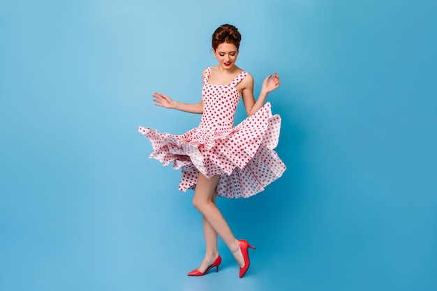 Vista completa de la mujer alegre bailando sobre fondo azul Pinup girl en vestido de lunares divirtiéndose