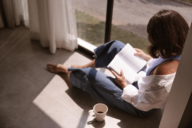 Vista completa de la mujer mirando el libro en el piso de su casa