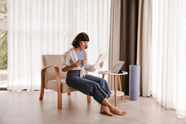 Vista completa de la mujer sentada en casa mirando en papel
