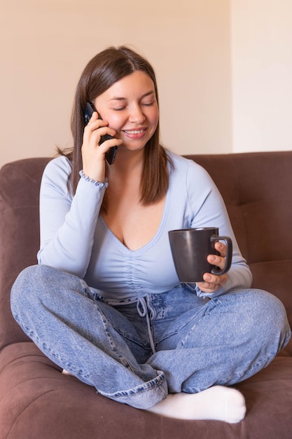 Vista completa de la mujer sonriente sentada en casa hablando por teléfono