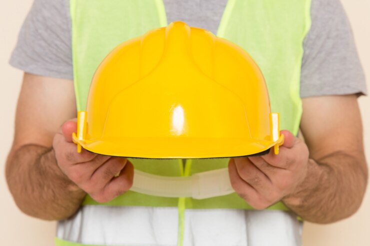 Foto gratuito vista delantera constructor masculino quitándose el casco amarillo en el fondo claro