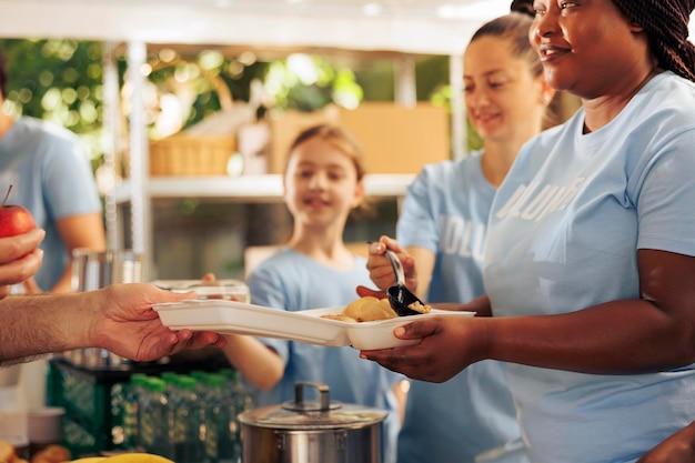 Vista detallada de los trabajadores de caridad que ayudan a las personas sin hogar, refugiados y necesitados mediante la distribución de alimentos gratuitos. Voluntarios amigables que sirven comidas, ofrecen apoyo y comparten artículos no perecederos.